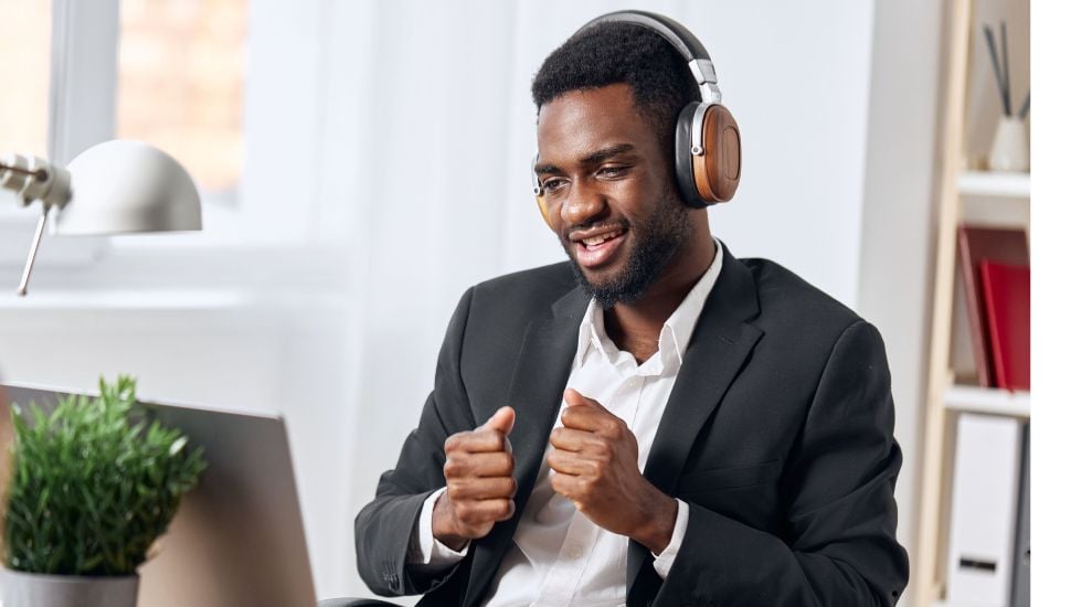 Black man in gray suit wearing headphones in front of laptop